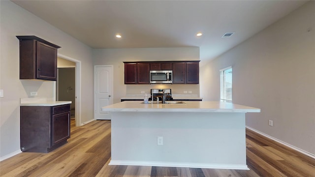 kitchen featuring dark brown cabinetry, a center island with sink, light hardwood / wood-style flooring, and sink