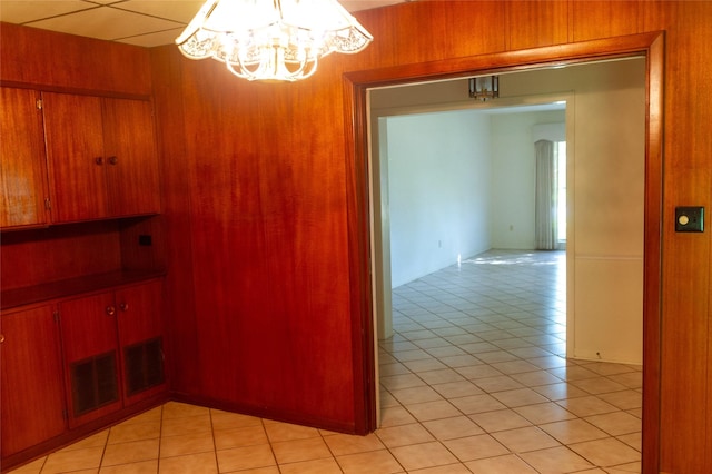 hallway featuring an inviting chandelier, light tile patterned floors, and wooden walls