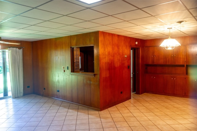 unfurnished room featuring a notable chandelier, light tile patterned flooring, and wood walls