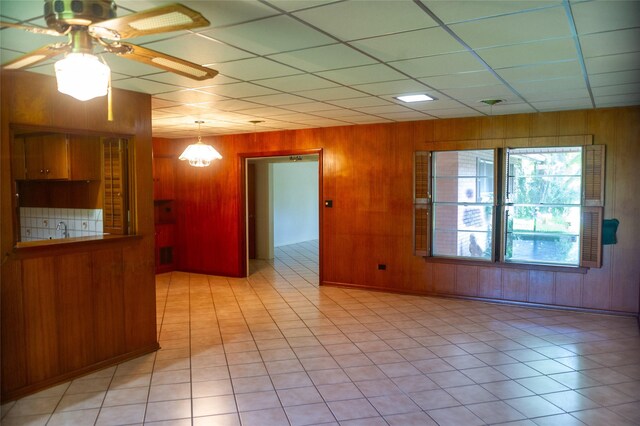 interior space featuring ceiling fan, wood walls, light tile patterned floors, and a drop ceiling