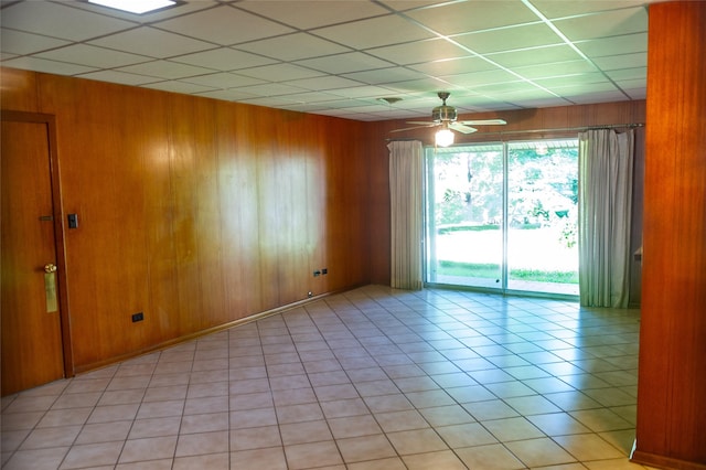 tiled empty room featuring ceiling fan, a paneled ceiling, and wooden walls