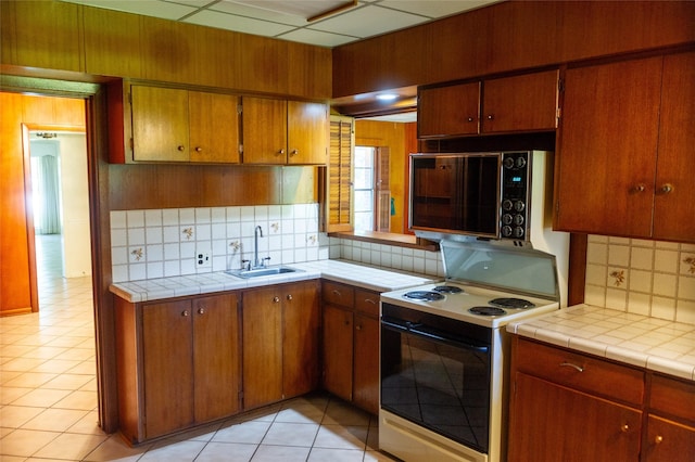 kitchen with sink, tile counters, backsplash, and electric stove