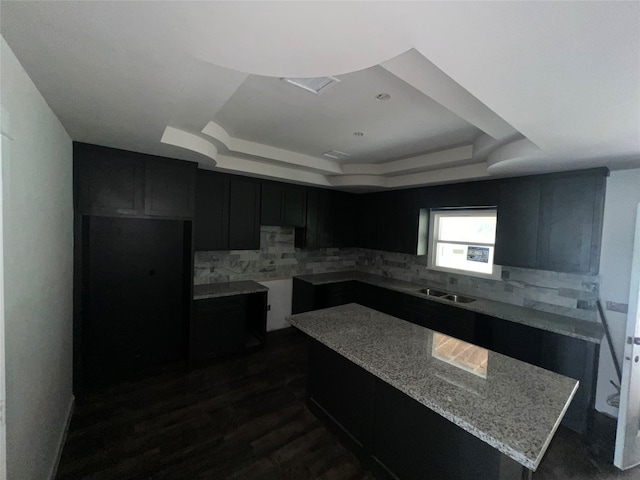 kitchen featuring light stone counters, a tray ceiling, dark hardwood / wood-style floors, and backsplash