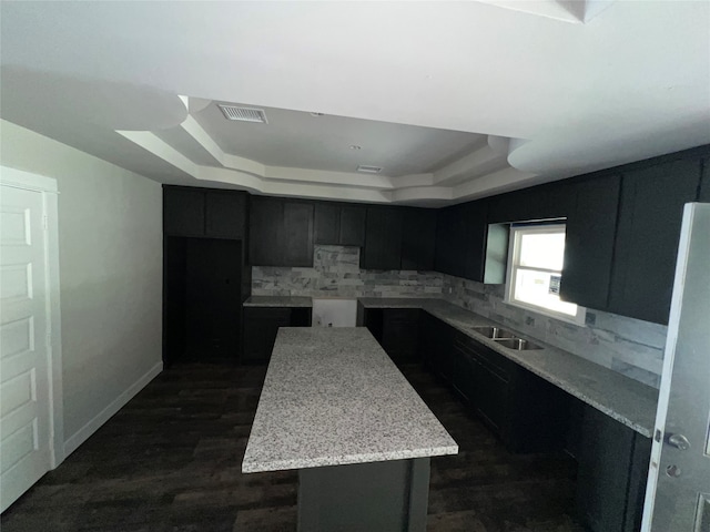 kitchen featuring tasteful backsplash, light stone countertops, dark hardwood / wood-style flooring, a tray ceiling, and a center island