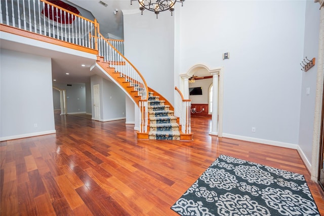 interior space with ornate columns, a high ceiling, an inviting chandelier, and hardwood / wood-style floors