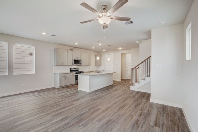 kitchen with stainless steel appliances, ceiling fan, pendant lighting, a center island with sink, and light hardwood / wood-style flooring