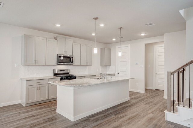 kitchen with a kitchen island with sink, light hardwood / wood-style flooring, hanging light fixtures, and appliances with stainless steel finishes