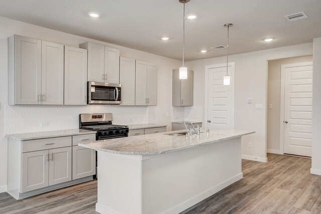 kitchen with a center island with sink, sink, light hardwood / wood-style flooring, appliances with stainless steel finishes, and decorative light fixtures