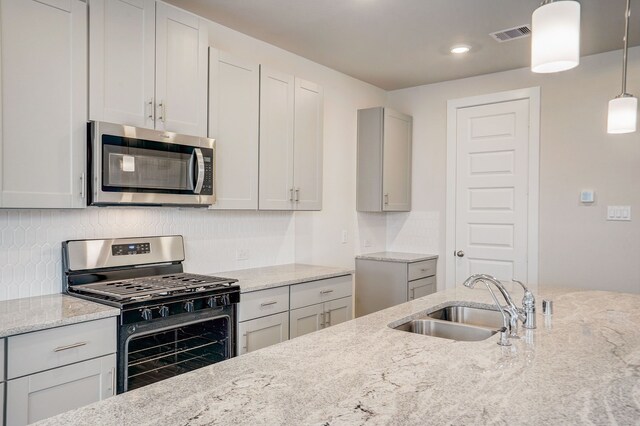 kitchen with light stone counters, sink, pendant lighting, and appliances with stainless steel finishes