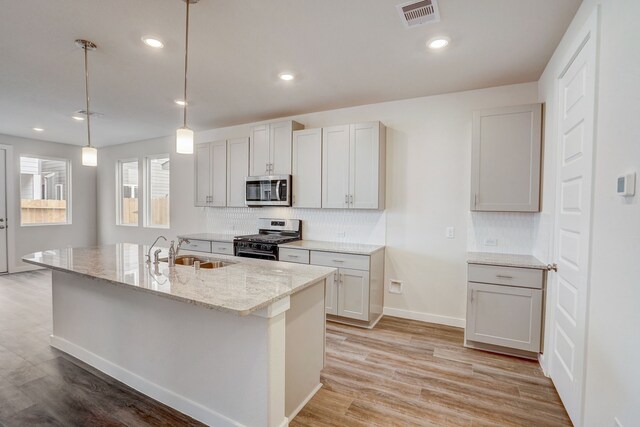 kitchen with light hardwood / wood-style flooring, sink, appliances with stainless steel finishes, and an island with sink