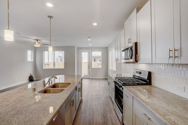 kitchen with appliances with stainless steel finishes, light wood-type flooring, light stone counters, sink, and white cabinetry