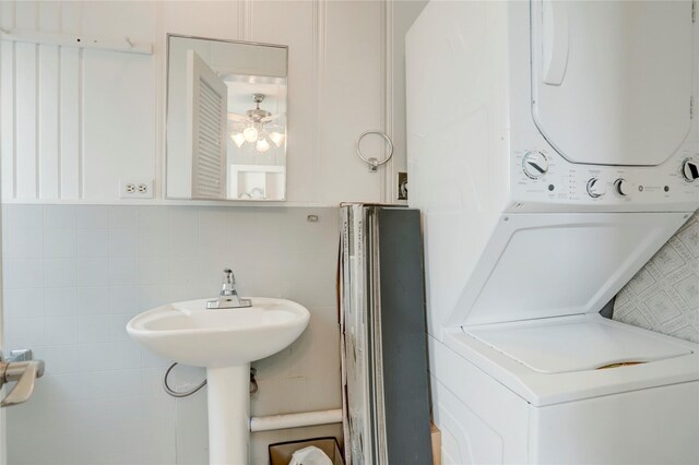 clothes washing area featuring tile walls, stacked washer and dryer, and ceiling fan