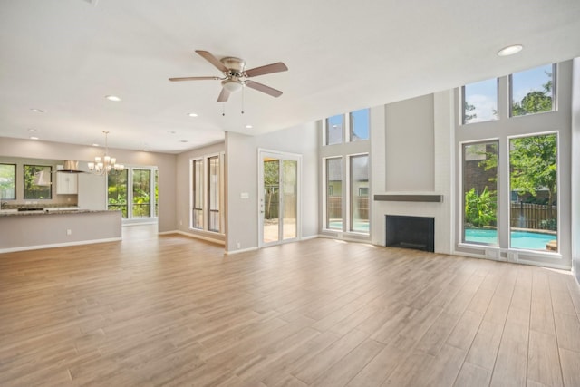 unfurnished living room featuring a wealth of natural light, light hardwood / wood-style flooring, and ceiling fan with notable chandelier