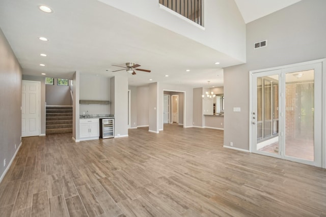 unfurnished living room featuring ceiling fan with notable chandelier, light hardwood / wood-style flooring, and wine cooler