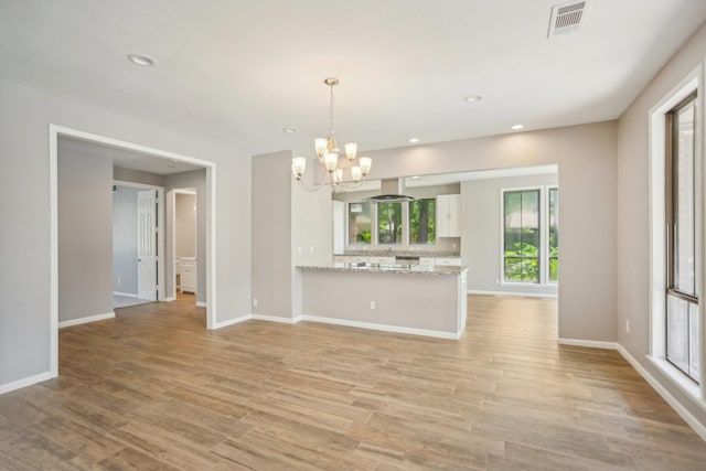 unfurnished living room featuring a chandelier and light hardwood / wood-style floors