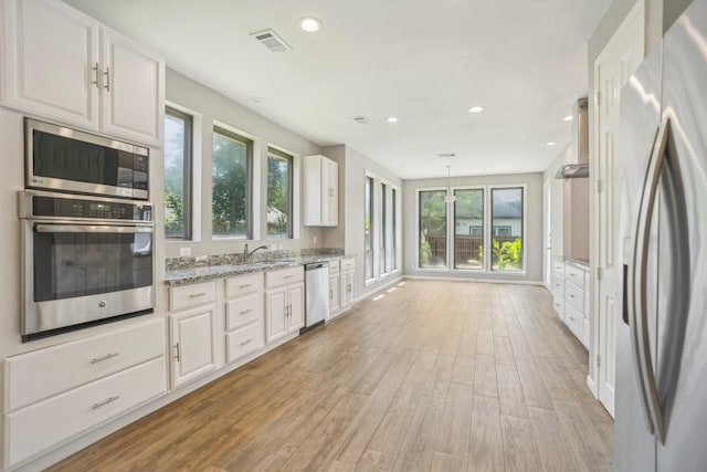 kitchen with light stone countertops, white cabinetry, hanging light fixtures, stainless steel appliances, and light wood-type flooring