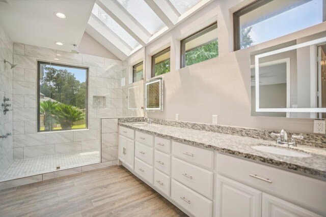 bathroom featuring a tile shower, a wealth of natural light, wood-type flooring, and lofted ceiling with skylight