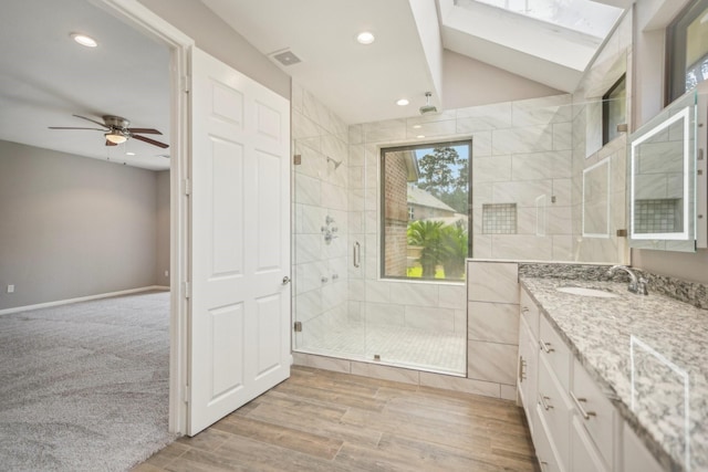 bathroom with vanity, hardwood / wood-style flooring, ceiling fan, vaulted ceiling with skylight, and a shower with shower door