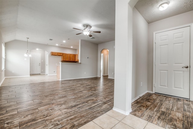 entryway featuring a textured ceiling, ceiling fan with notable chandelier, light hardwood / wood-style flooring, and vaulted ceiling