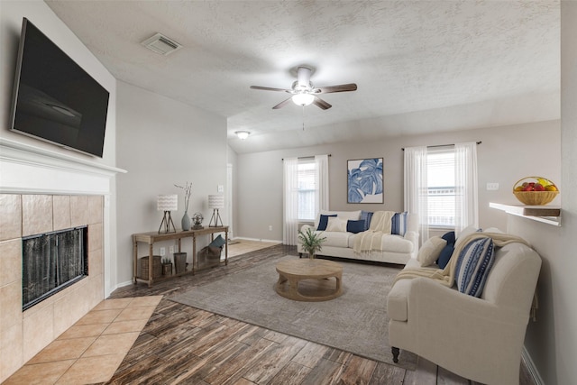 living room with light wood-type flooring, a textured ceiling, ceiling fan, a fireplace, and lofted ceiling