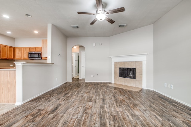 unfurnished living room featuring dark hardwood / wood-style floors, ceiling fan, and a tiled fireplace