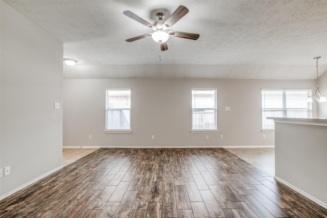 spare room with a textured ceiling, ceiling fan with notable chandelier, a wealth of natural light, and dark wood-type flooring