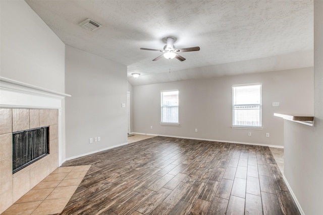 unfurnished living room featuring vaulted ceiling, ceiling fan, a textured ceiling, a fireplace, and light hardwood / wood-style floors