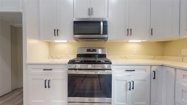 kitchen featuring stainless steel appliances, wood-type flooring, white cabinets, and light stone countertops