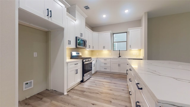 kitchen with light stone countertops, stainless steel appliances, light hardwood / wood-style flooring, and white cabinetry