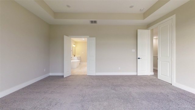 unfurnished bedroom with ensuite bath, a raised ceiling, and carpet flooring