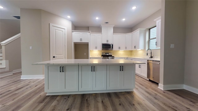 kitchen featuring appliances with stainless steel finishes, white cabinetry, a center island, and light hardwood / wood-style flooring