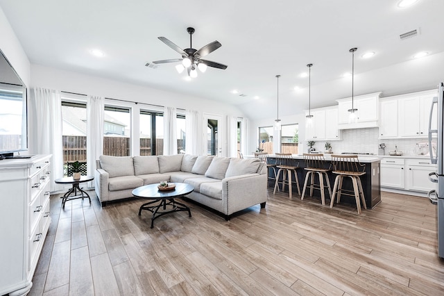 living room with ceiling fan, light hardwood / wood-style flooring, and vaulted ceiling