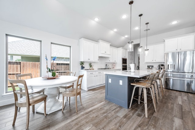 kitchen with decorative light fixtures, vaulted ceiling, white cabinetry, appliances with stainless steel finishes, and an island with sink