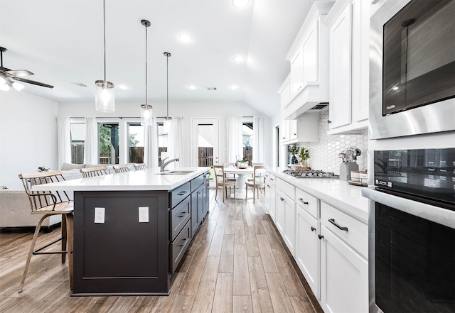 kitchen featuring a center island with sink, stainless steel appliances, a kitchen bar, and white cabinets