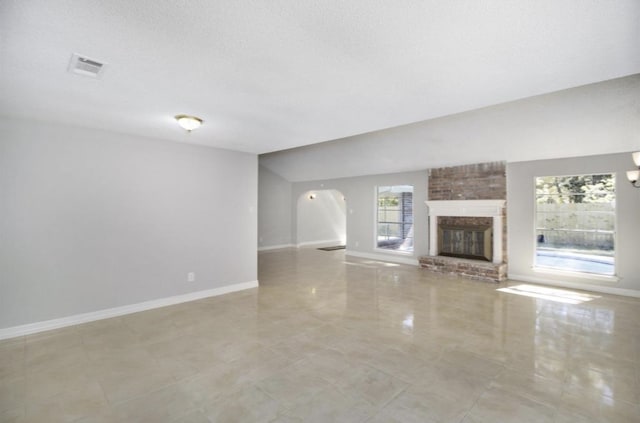 unfurnished living room with brick wall, a brick fireplace, a textured ceiling, and light tile floors