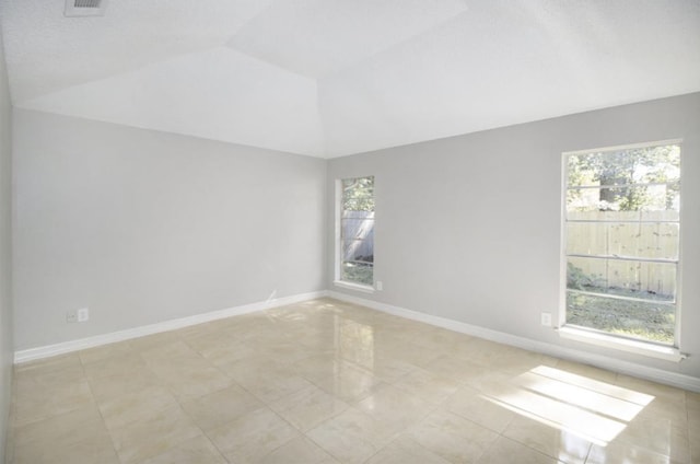 spare room with plenty of natural light, vaulted ceiling, and light tile floors