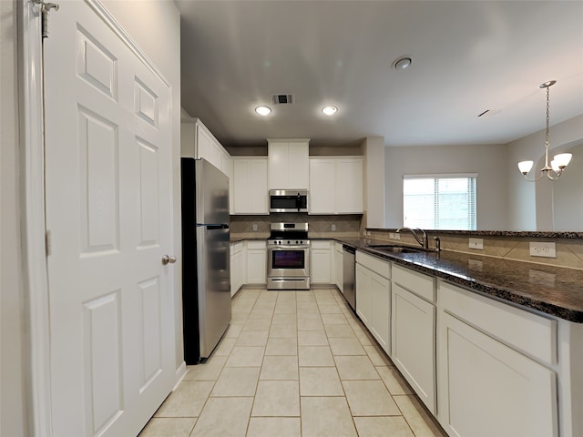 kitchen with hanging light fixtures, sink, dark stone countertops, appliances with stainless steel finishes, and white cabinetry