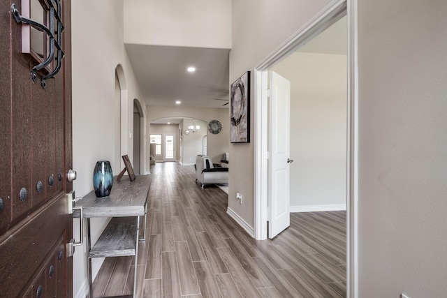 corridor with arched walkways, wood finish floors, recessed lighting, and baseboards