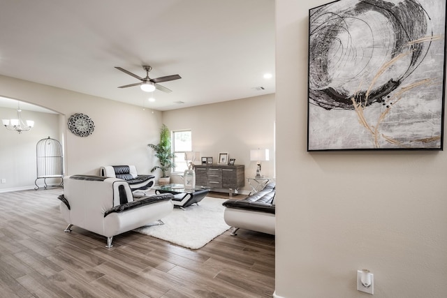 living area featuring ceiling fan with notable chandelier, visible vents, baseboards, and wood finished floors