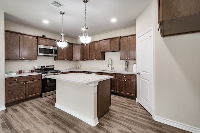 kitchen featuring a kitchen island, stainless steel appliances, wood-type flooring, sink, and pendant lighting