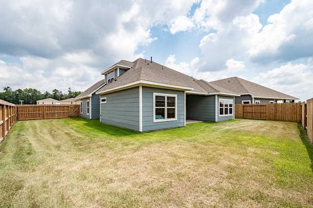 back of house featuring a fenced backyard, roof with shingles, and a yard