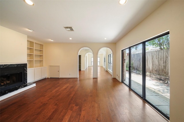 unfurnished living room featuring a fireplace, built in features, and dark wood-type flooring