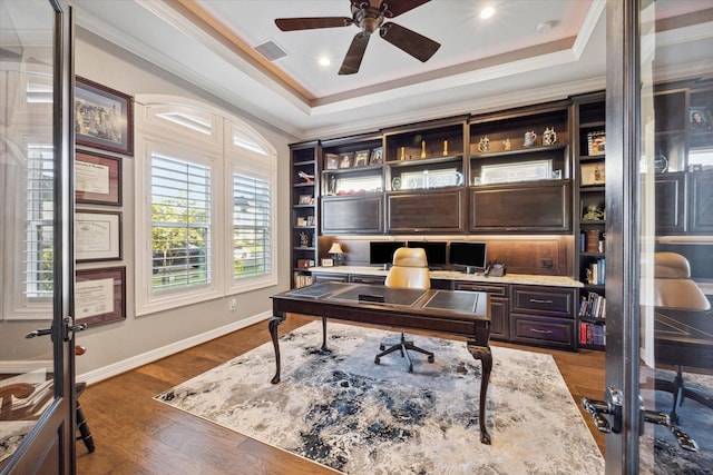 office space with a raised ceiling, ceiling fan, dark wood-type flooring, and ornamental molding