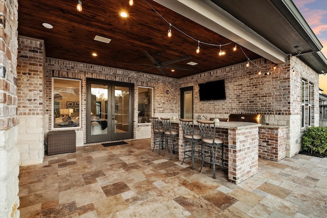 patio terrace at dusk featuring an outdoor kitchen, a grill, an outdoor bar, and french doors