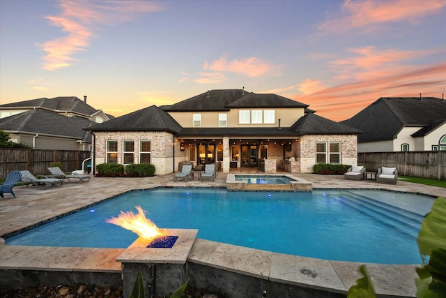 pool at dusk featuring an in ground hot tub, a patio, and an outdoor fire pit