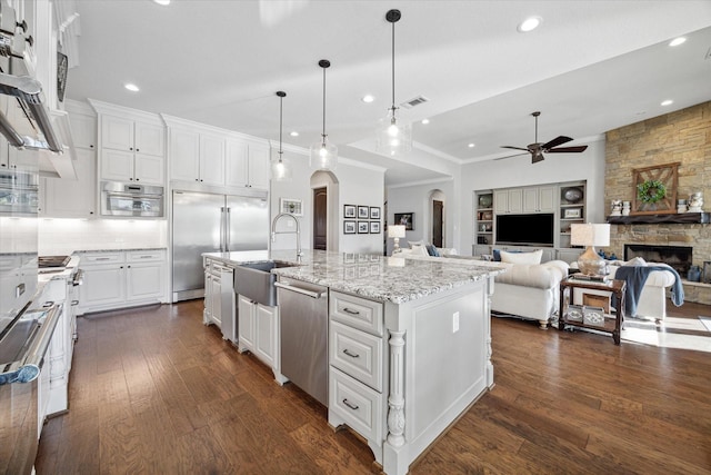 kitchen with appliances with stainless steel finishes, pendant lighting, a center island with sink, a fireplace, and white cabinetry