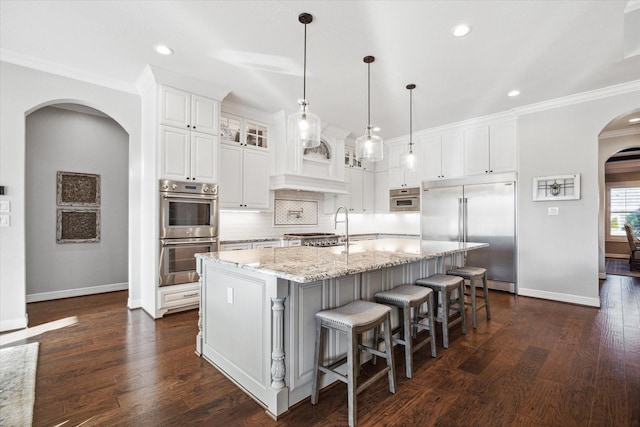 kitchen with appliances with stainless steel finishes, backsplash, light stone counters, white cabinets, and an island with sink