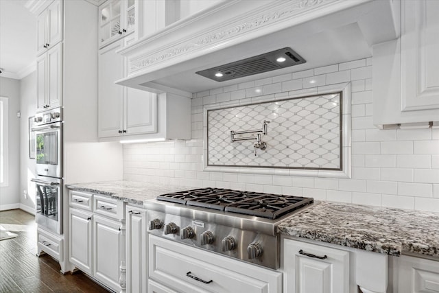 kitchen featuring decorative backsplash, white cabinetry, light stone counters, and appliances with stainless steel finishes