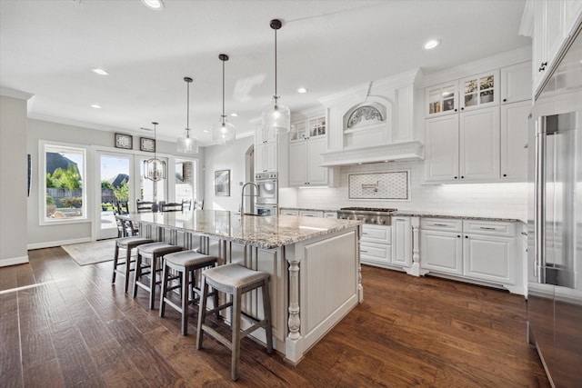 kitchen with pendant lighting, a kitchen bar, a kitchen island with sink, white cabinets, and light stone counters