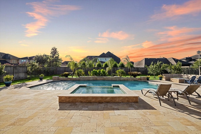 pool at dusk featuring an in ground hot tub, pool water feature, and a patio